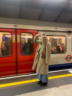 a woman standing in front of a train at a subway station with her hand on her head