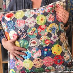 a woman holding up a colorful patchwork pillow