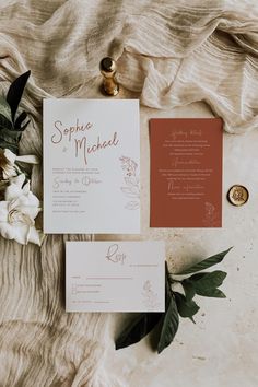 the wedding stationery is laid out on top of the bed sheet and flowers are placed next to it