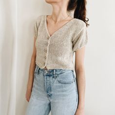 a woman standing in front of a white wall wearing jeans and a knitted cardigan