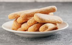 a white bowl filled with sugar covered doughnuts on top of a gray table