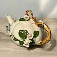 a ceramic teapot with flowers painted on the front and sides, sitting on a wooden table