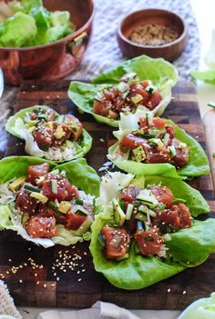 lettuce wraps with meat and vegetables on a cutting board next to bowls of seasoning