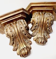 two ornate gold wood brackets on a white surface