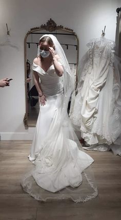 a woman in a white wedding dress standing next to a mirror and looking at her face