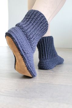 a woman's feet wearing blue knitted slippers and socks on top of a wooden floor