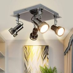 three spotlights are on the ceiling above a table with a potted plant in it