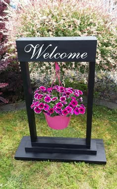 a welcome sign with purple flowers in a pink flower pot sitting on a black stand