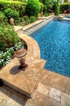 an outdoor swimming pool surrounded by greenery and flowers in a backyard area with stone steps leading up to it