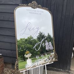 a large mirror sitting on top of a white stand next to a black building with a sign that says, welcome to the wedding of lacy and lily