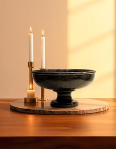 two candles are lit in a black bowl on a wooden table next to a candle holder