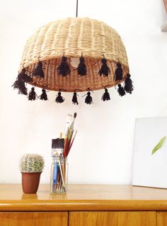 a basket hanging from the ceiling with tassels on it next to a potted plant