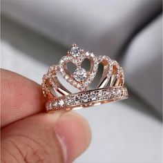 a hand holding a ring with a crown on it's side and diamonds in the middle