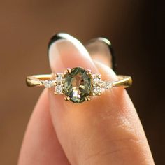 a close up of a person's hand holding a ring with an oval shaped green stone