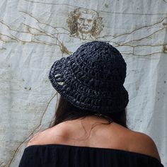 a woman wearing a black crochet hat looking at a drawing on the wall