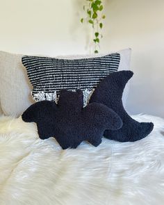 two black pillows sitting on top of a white bed next to a pillow with an animal design