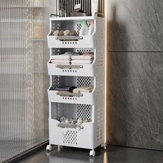 a white storage rack with four baskets on wheels in front of a marble tiled wall