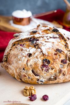 a loaf of bread sitting on top of a cutting board next to nuts and cranberries