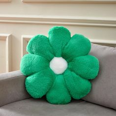 a green flower shaped pillow sitting on top of a gray couch next to a wall