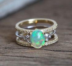 an opal and diamond ring set on top of a wooden table with other rings