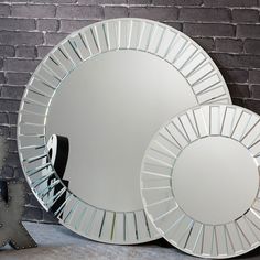 two round mirrors sitting next to each other on the ground in front of a brick wall