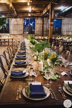 the long table is set with place settings and blue napkins, silverware, and greenery