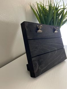 a black wooden box with two keys on it and a plant in the corner next to it