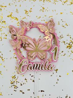 a pink and gold cake topper with butterflies on it