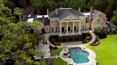 an aerial view of a large house with a pool in the front yard and trees surrounding it