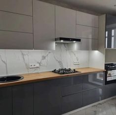 a kitchen with marble counter tops and grey cupboards, along with a black stove top oven