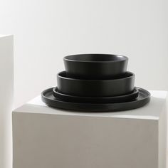 three black plates stacked on top of each other in front of a white wall and pedestal