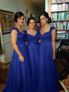 three women in blue dresses posing for the camera with bookshelves in the background