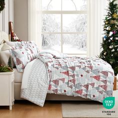 a bed room with a neatly made bed and a christmas tree in front of a window