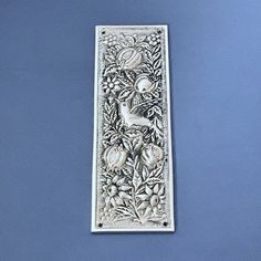 an ornate metal plaque with birds and flowers on it's side, against a blue background