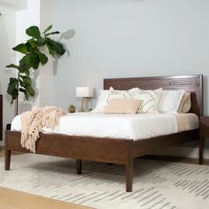 a bed with white sheets and pillows in a room next to a potted plant