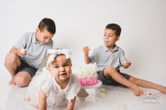 two young children sitting on the floor in front of a cake