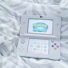 a nintendo wii game system sitting on top of a white bed covered in blankets and sheets