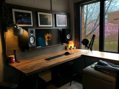 a desk with speakers and pictures on the wall next to a window that looks out onto trees