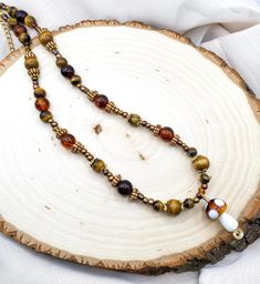 This one of a kind beaded necklace is perfect for anyone who loves mushrooms, nature, or the fairy and goblincore aesthetic. It is 17 inches long and has a 4.5 inch extender chain, making it 21.5 inches total. This necklace was designed and hand crafted with genuine tiger's eye crystal beads, dark brown wood beads, and a variety of other beads. Such as gold spacer beads, gold bead caps, and other pretty brown glass and plastic beads. In the center of the necklace hangs a glass mushroom pendant, with a gold wire swirl on the bottom of it. The ends are secured with crimp beads and crimp bead covers, and the necklace is attachable with a lobster claw clasp. All metals used in this necklace are hypoallergenic, lead and nickel free.  This necklace is handmade so please handle with care.<3 Tiger Goblincore Necklace, Fairy Nature, Mushrooms Nature, Wood Beads Jewelry, Tigers Eye Crystal, Necklace Gold Jewelry, Crimp Bead Covers, Goblincore Aesthetic, Mushroom Necklace