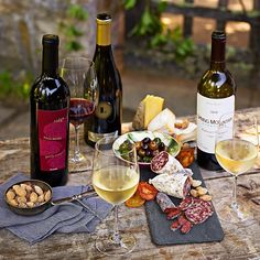 three bottles of wine, two glasses of wine and some food on a wooden table