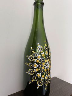 a green bottle with yellow and white flowers painted on it sitting on a wooden shelf