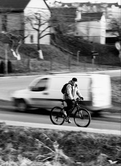 a man riding a bike down a street next to a white van and grass in front of him