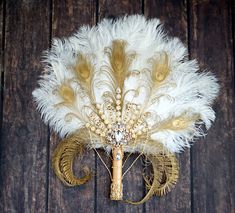 a white and gold brooch with feathers on it's back, sitting on a wooden surface