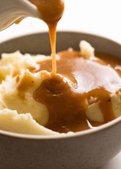 a spoon drizzling sauce over mashed potatoes in a bowl with gravy