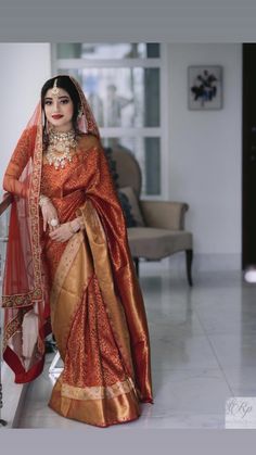 a woman in an orange and gold sari poses for the camera with her hand on her hip