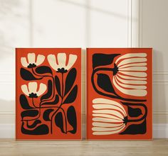 two orange and black paintings sitting on top of a wooden floor