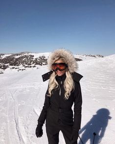 a woman standing in the snow wearing skis and a fur lined hood on her head