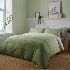 a bed with green sheets and pillows next to a window