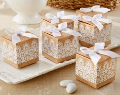 four small boxes with white lace on them sitting on a plate next to some flowers