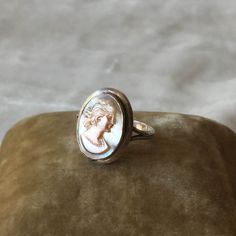 This is such a beautiful ring! It has an oval shaped carved cameo of a woman in profile, with a carved necklace on her neck and shoulder length hair. The cameo looks to be carved of mother of pearl or shell. The cameo is pink with a soft toned blue grey background Maker: Unknown Age: Unknown, estimated to between 1900-1940 Color: Silver, peach pink, blue grey Material: The metal is unmarked but acid tests to sterling. Cameo is shell or mother of pearl, carved. Condition: There's a small area of Elegant Carved Oval Jewelry, Elegant Oval Carved Jewelry, Elegant Oval Cameo Jewelry, Carved Oval Jewelry For Wedding, Oval Carved Jewelry For Wedding, Elegant Carved Oval Jewelry For Wedding, Round Intaglio Jewelry, Engraved Heirloom Rings, Formal Oval Mother Of Pearl Rings